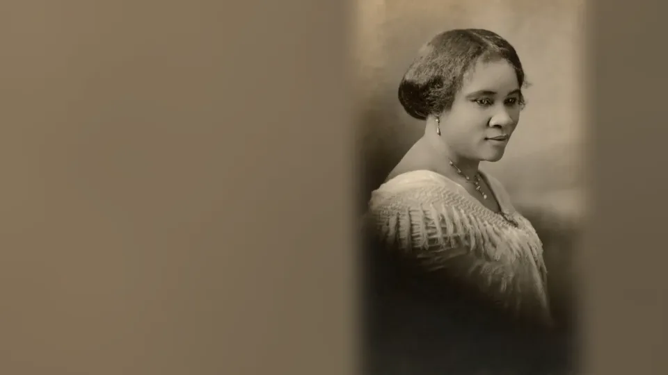 Retrato de estudio, en sepia, de Madam C. J. Walker (hacia 1914), de perfil tres cuartos y mirada baja, con collar y blusa de encaje. Fotografía histórica.